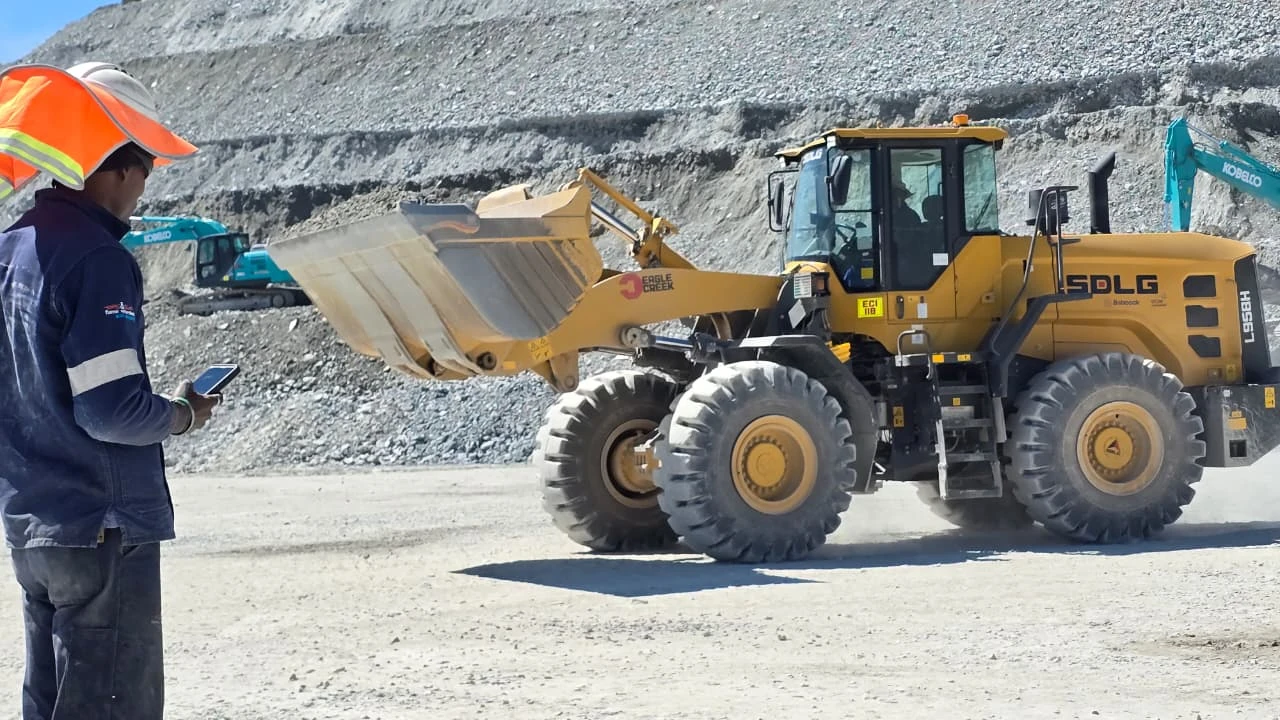 An operator using a handheld device beside a loader at a working quarry